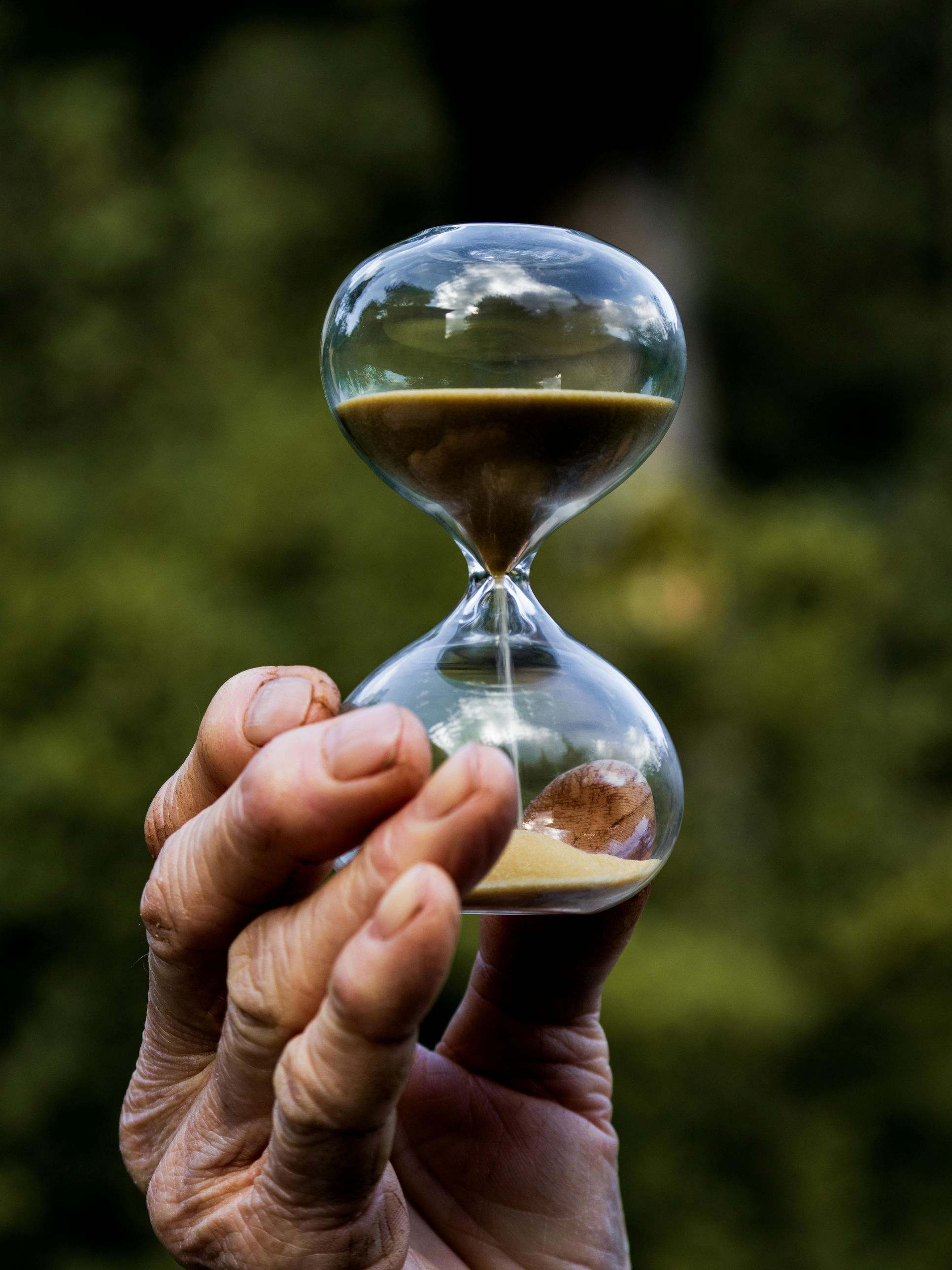 A hand holding an hourglass, sand still falling, the value of getting in quickly.